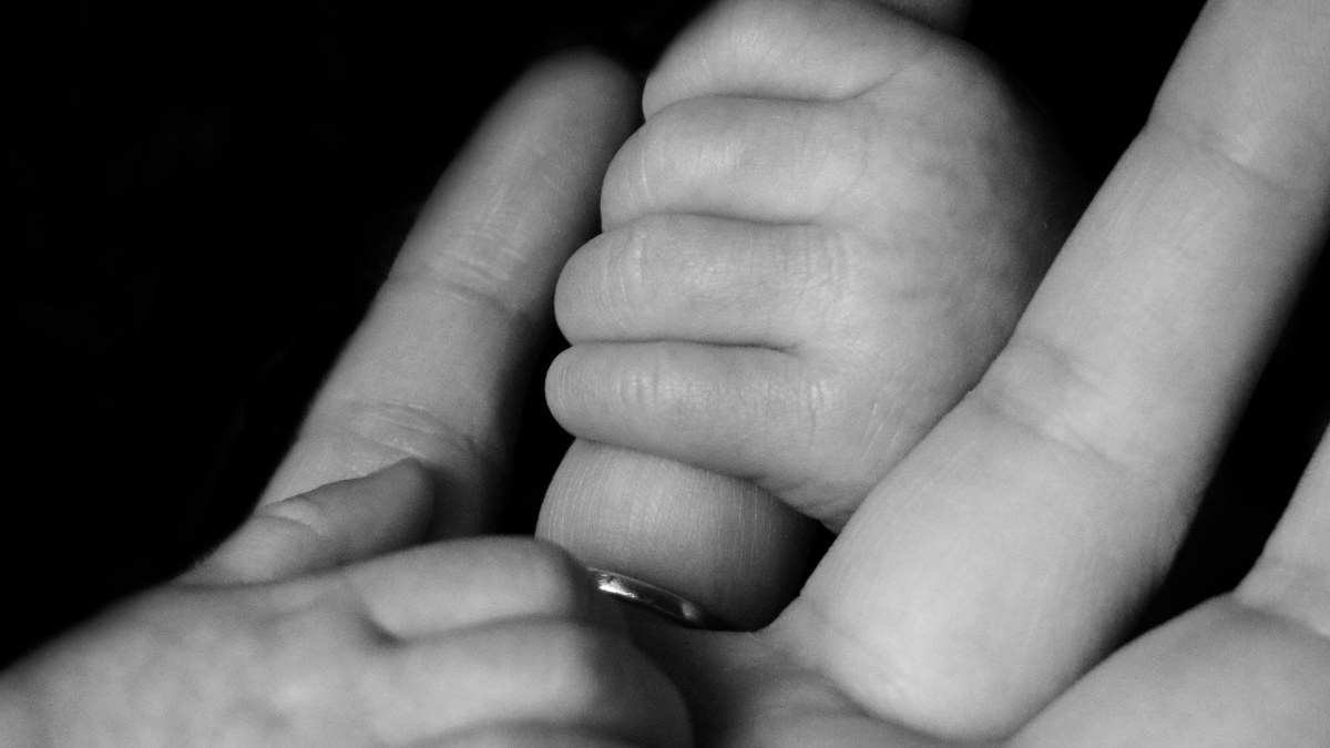 
a baby with her hands on the palm of her mother symbolyzing the parental bond and the crushing responsibility of parenthood
