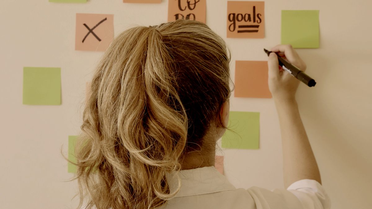 
a blonde woman writing on a wall with sticky notes creating goals by natalia blauth
