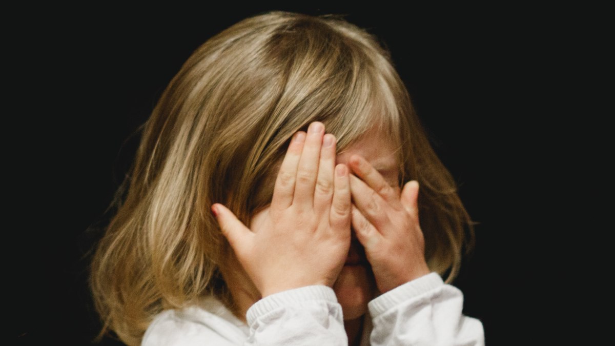 
a child covering their eyes signifying an intolerance for social flexibity and stunted cognitive ability both
