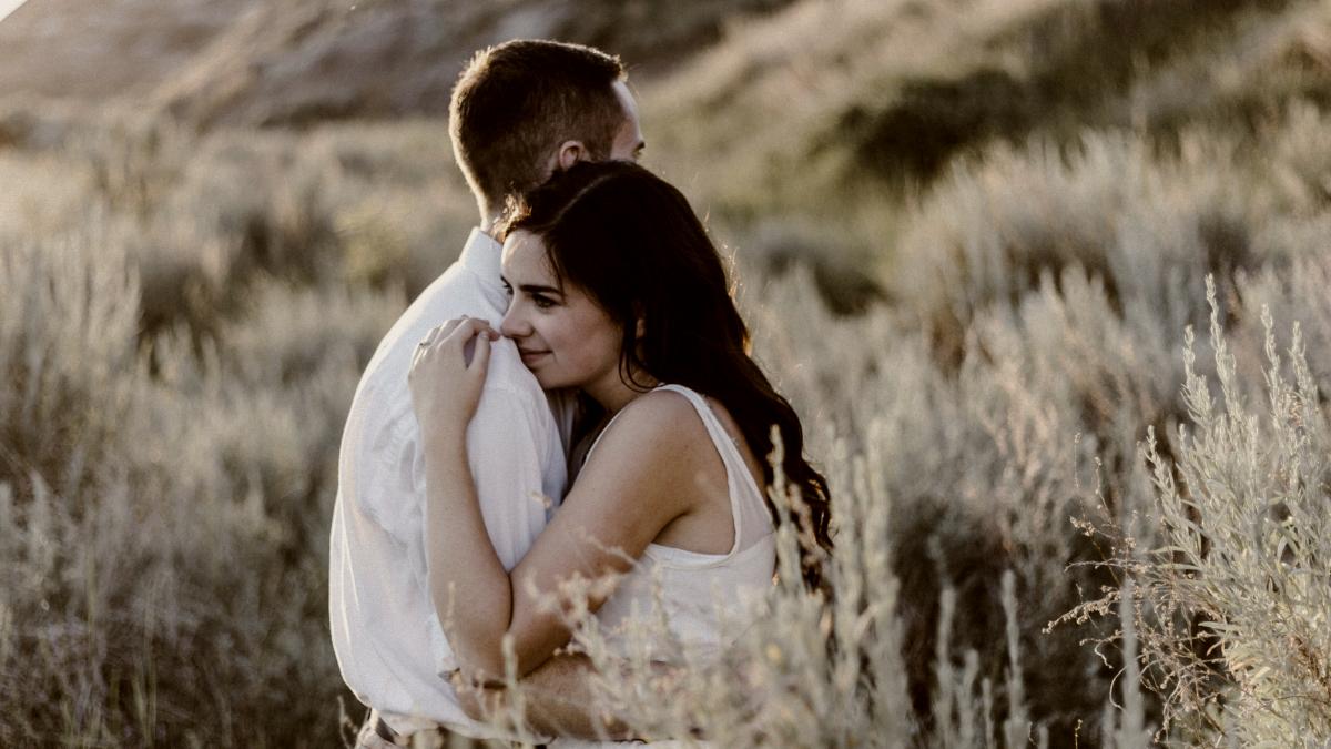 
a-couple-higging-in-a-field-near-a-mountain
