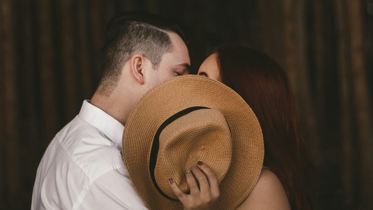 
a-couple-kissing-behind-a-hat
