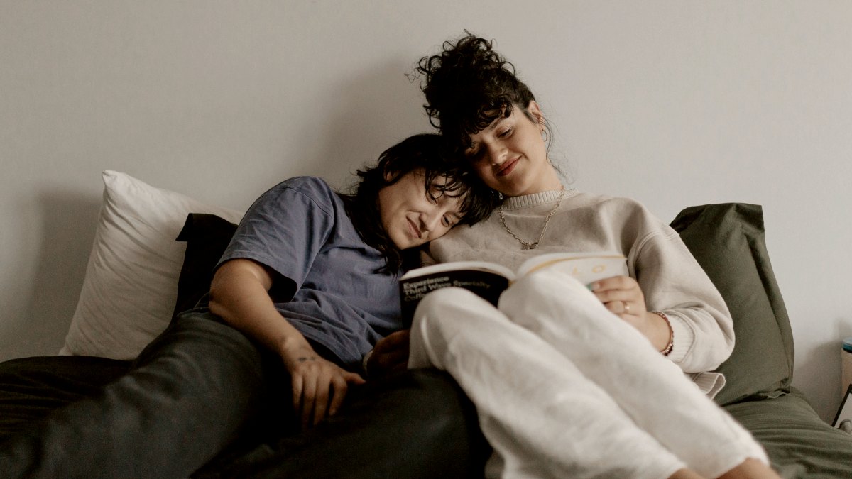 
a couple laying on top of a bed reading together
