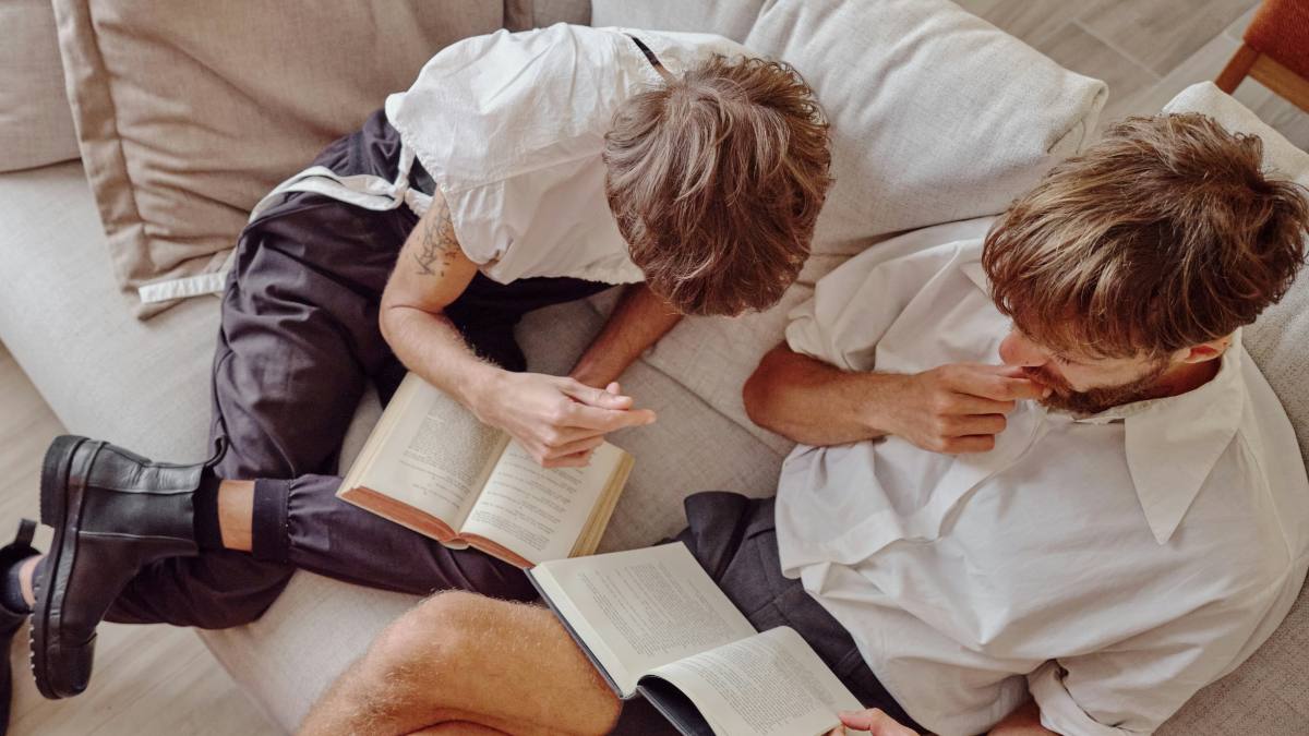 
a couple sitting on top of a couch reading their books next to each other
