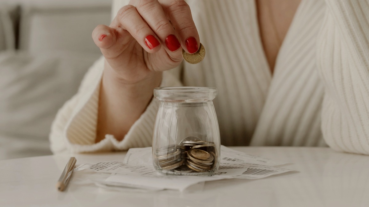 
a crying woman sitting at a table with a jar of coins
