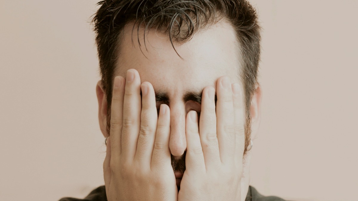 
a depressed man covering his eyes with his hands
