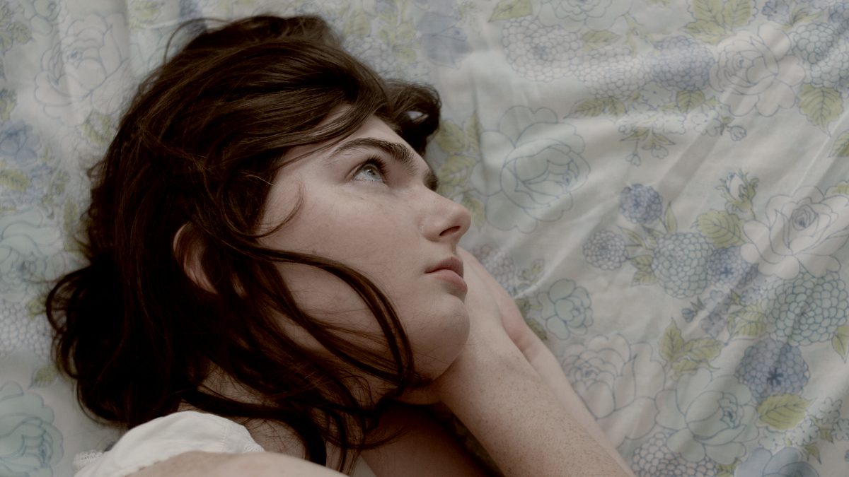 
a freckled brunette woman lying on top of a blue floral print bed, thinking by Gabriel Ponton
