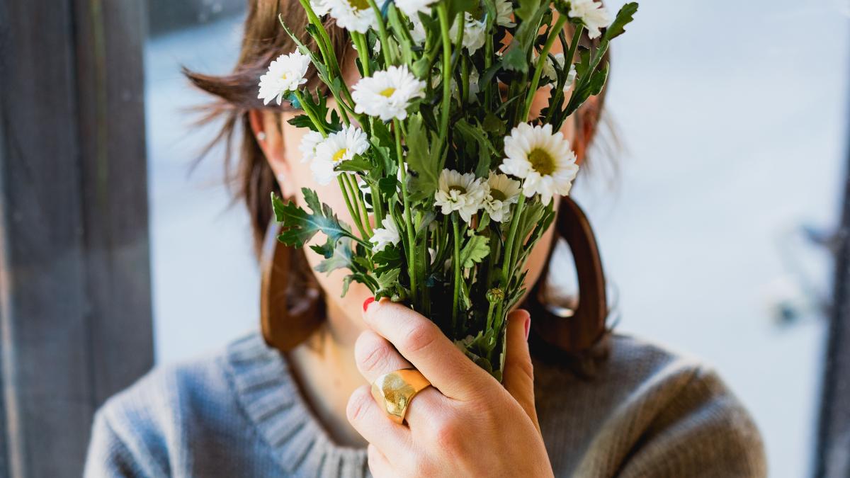 
a girl hiding her face with flowers she got for a date symbolyzing dating anxiety and a fear of opening up
