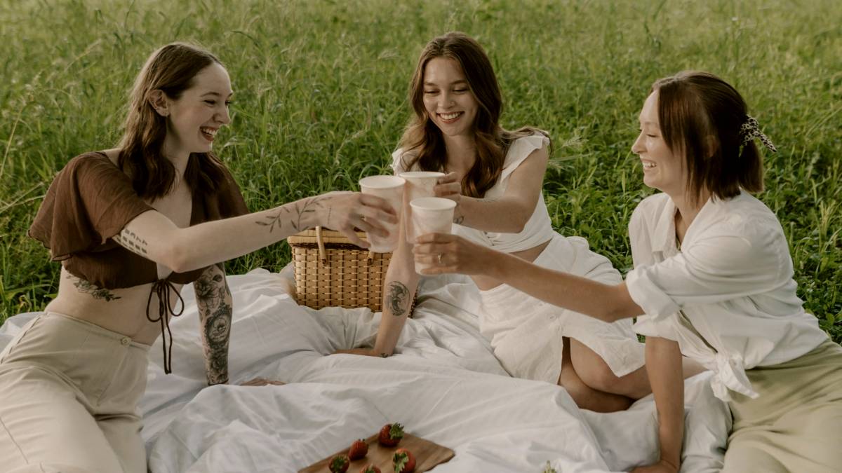 
a group of women sitting on top of a lush green field having a picnic
