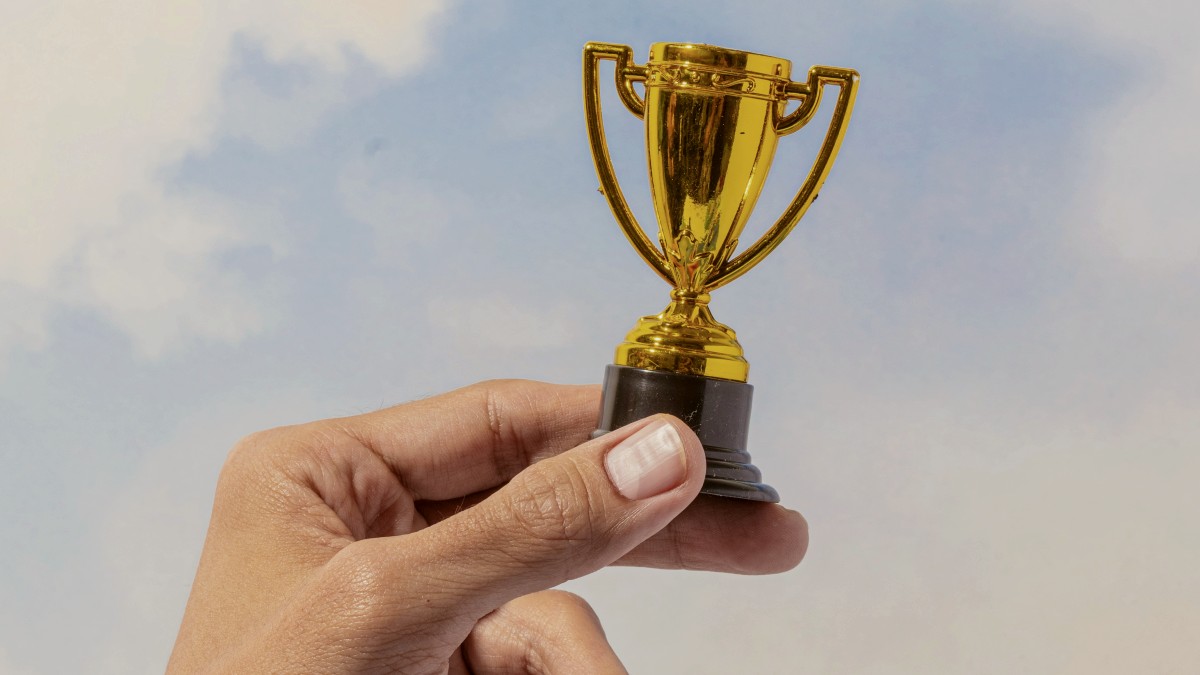 
a hand holding a gold trophy against a blue sky by Katelyn Perry
