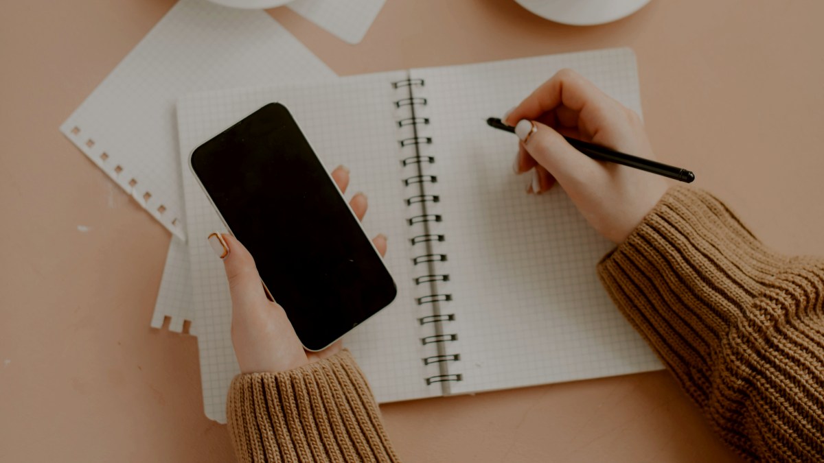 
a hand holding a pen and a phone next to a cup of coffee
