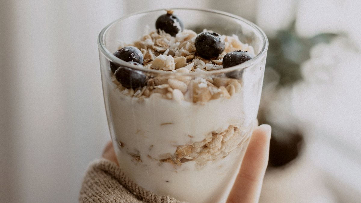 
a hand holding overnight oats in a clear drinking glass
