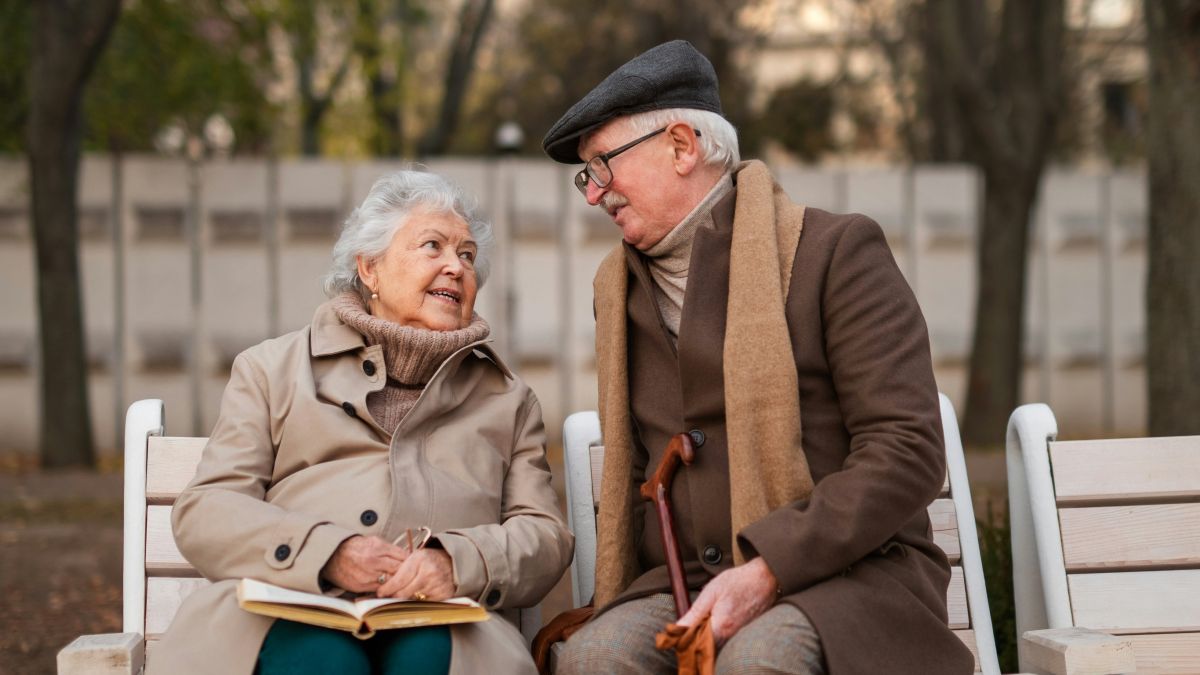 
A happy senior friends on sitting on bench and talking outdoors in park on autumn day by Getty Images
