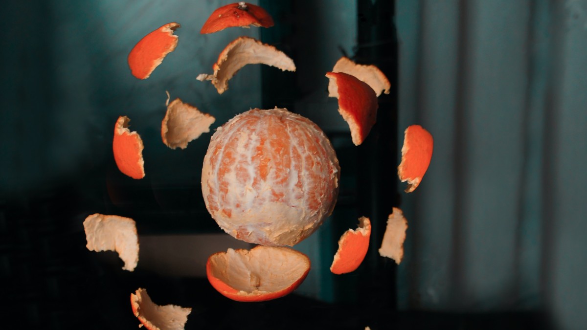 
a levitating orange and small pieces of peels floating around coming together 
