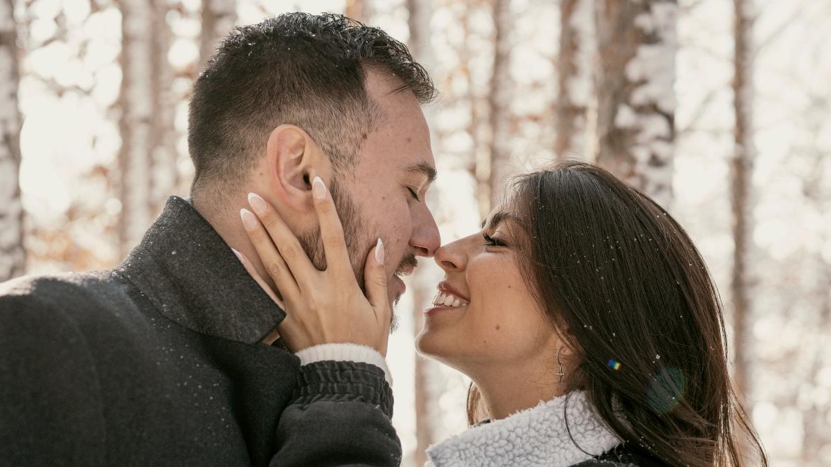 
a man and a woman about to kiss under the falling snow

