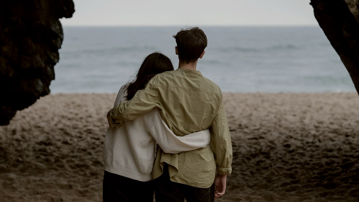 
a man and a woman are walking on the beach with their backs facing the camera
