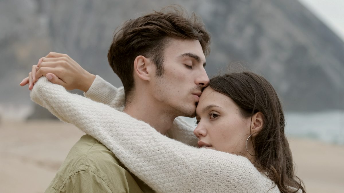 
a man and a woman embracing on the beach while looking into the distance
