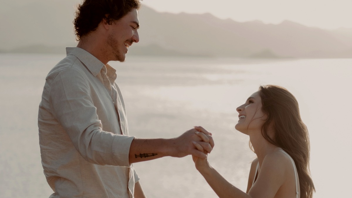 
a man and a woman holding hands near the water
