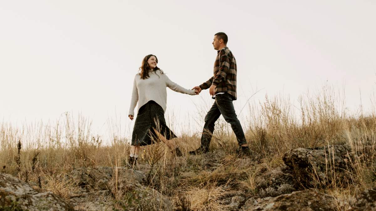 
a man and a woman holding hands walking across a field
