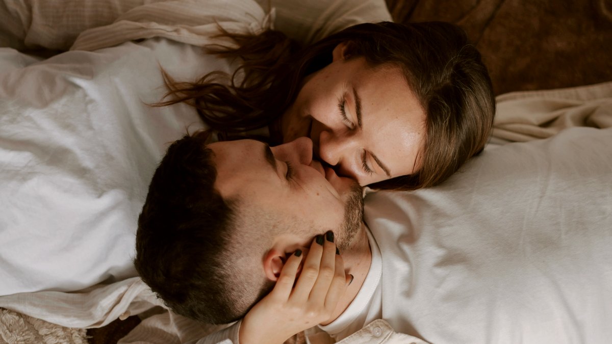 
a man and a woman laying on a bed together about to kiss
