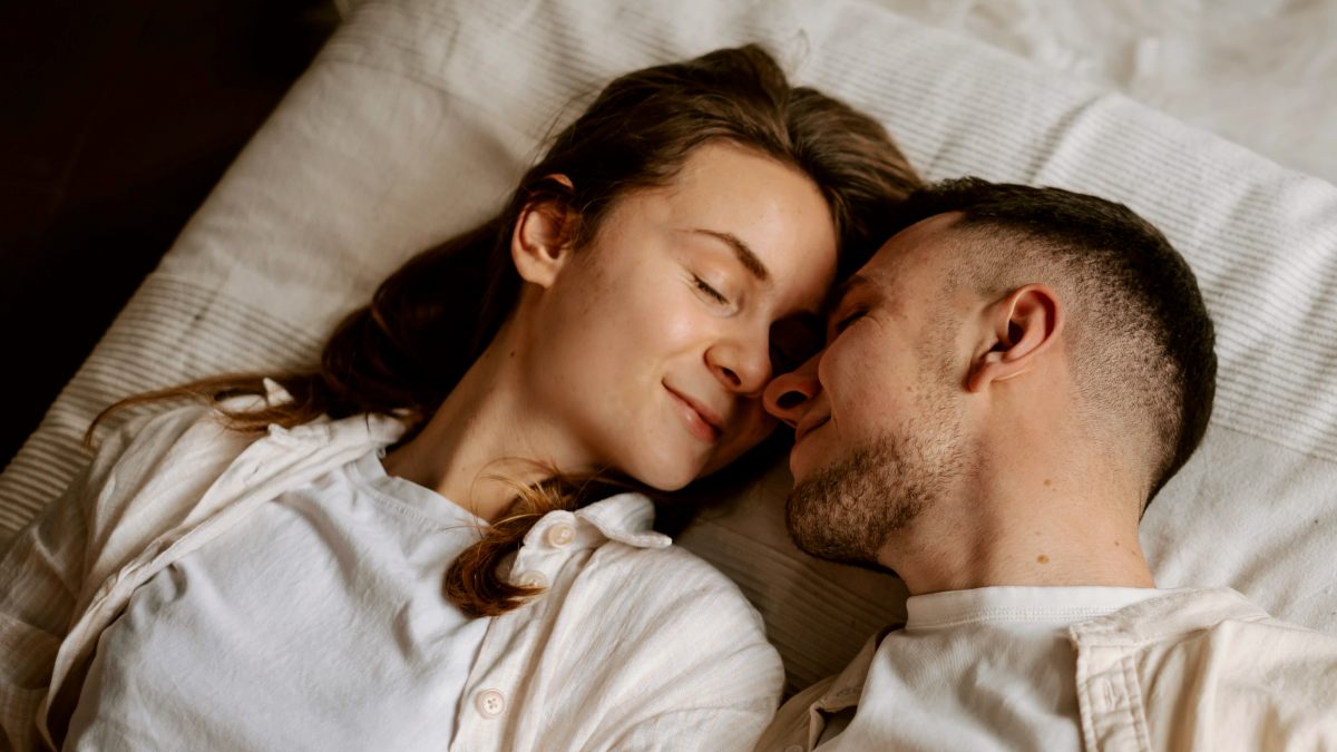 
a man and a woman laying on a bed together with their foreheads together
