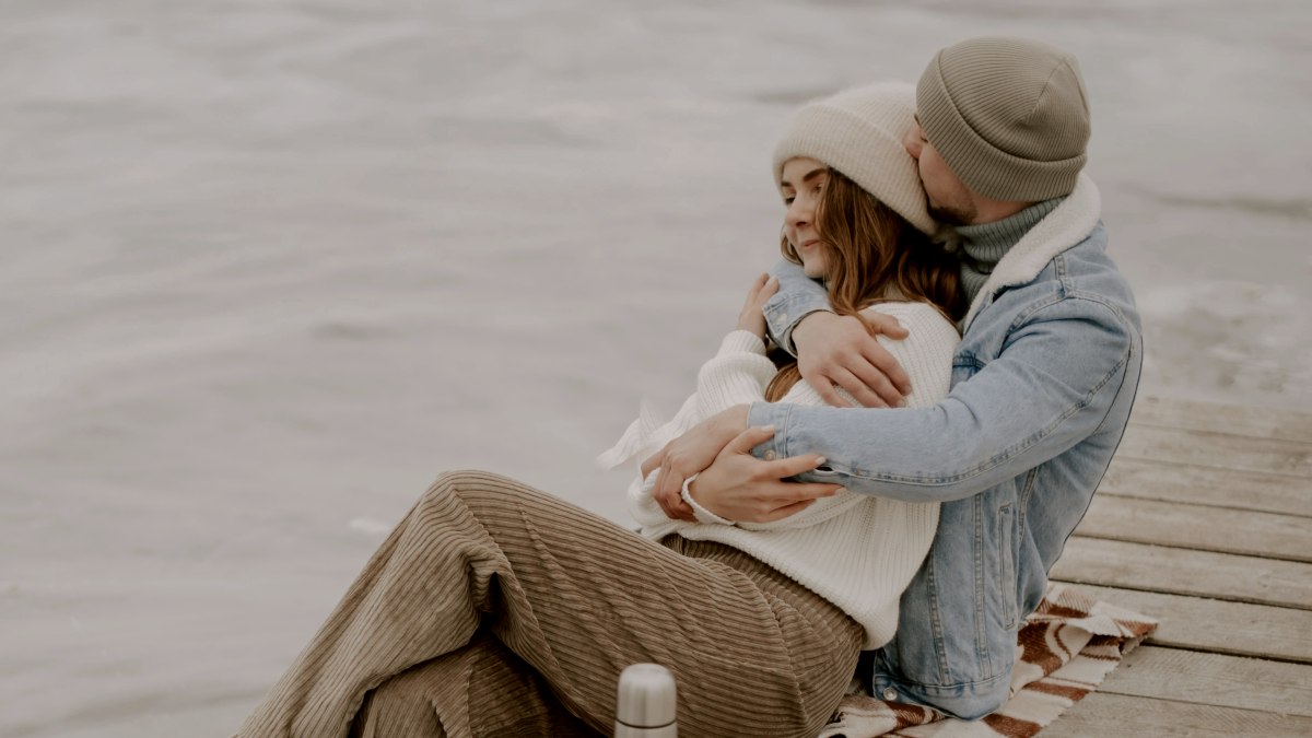 
a man and a woman sitting on a dock next to a frozen lake cuddling
