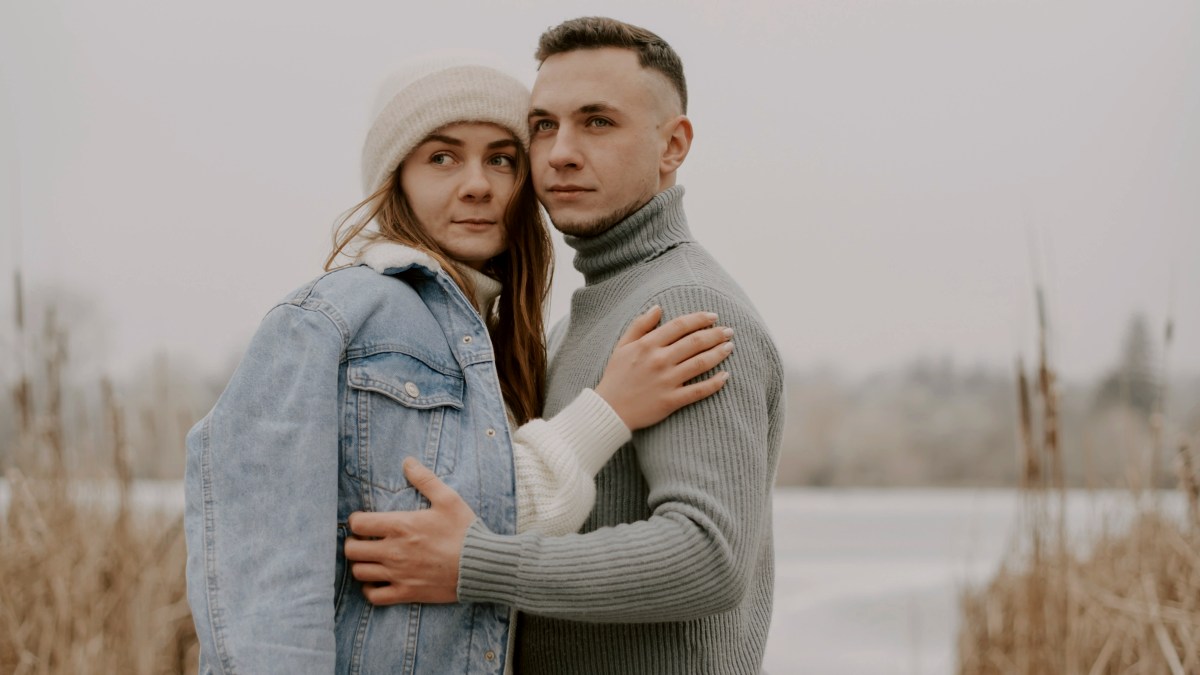 
a man and a woman standing next to each other in front of a frozen lake
