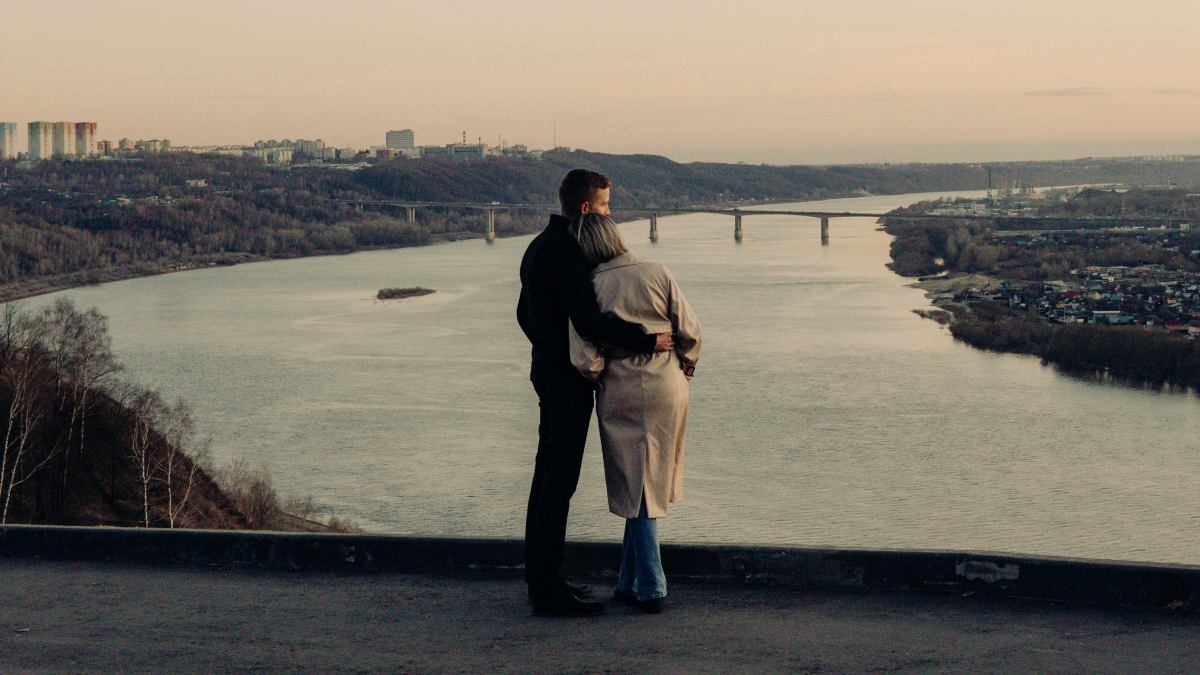 
a man and a woman standing on a hill overlooking a body of water
