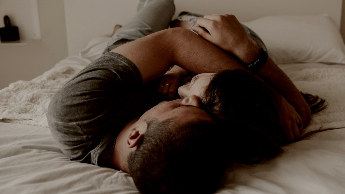 
A man and woman cuddling together in bed on white sheets by Becca Tapert
