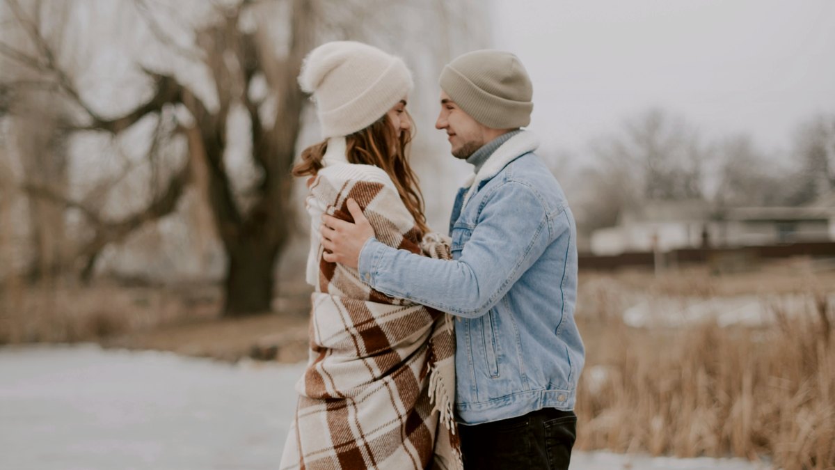 
a man and woman standing face to face on a dock next to a body of water wearing winter clothes by Kateryna Hliznitsova
