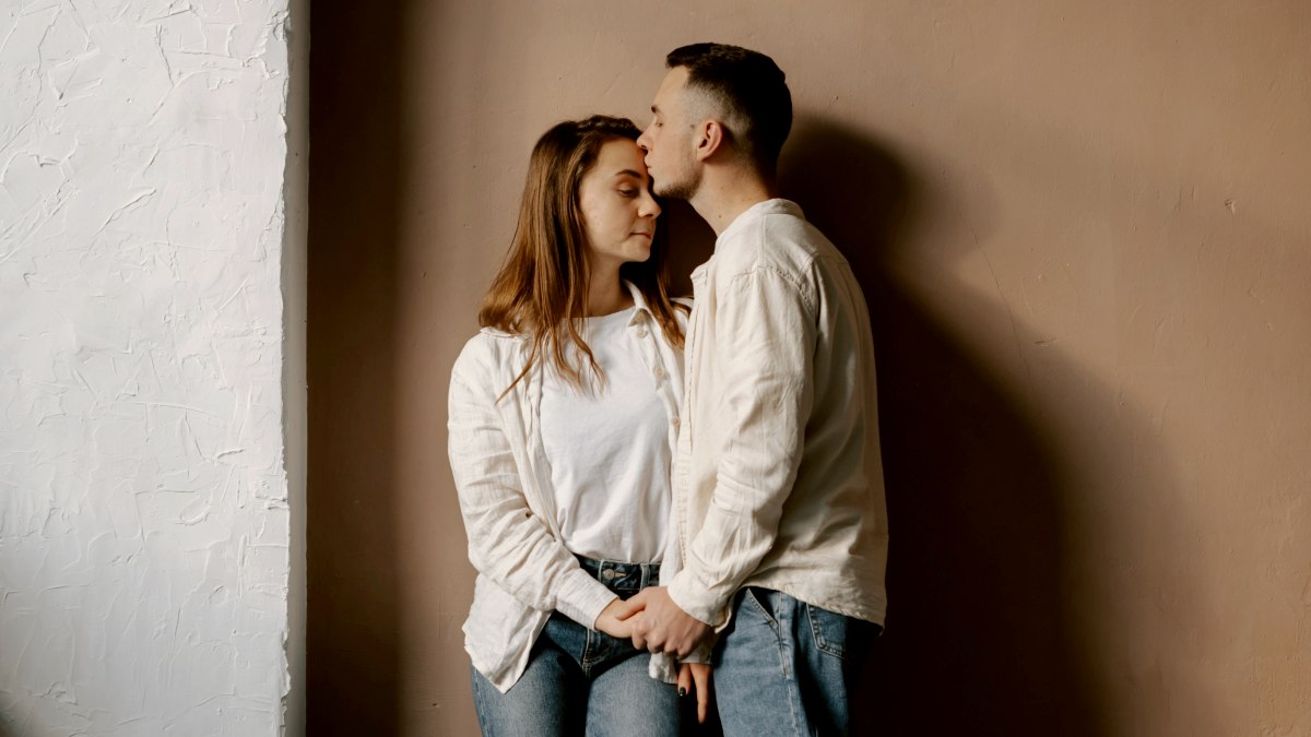 
a man and woman standing next to each other in front of an orange wall
