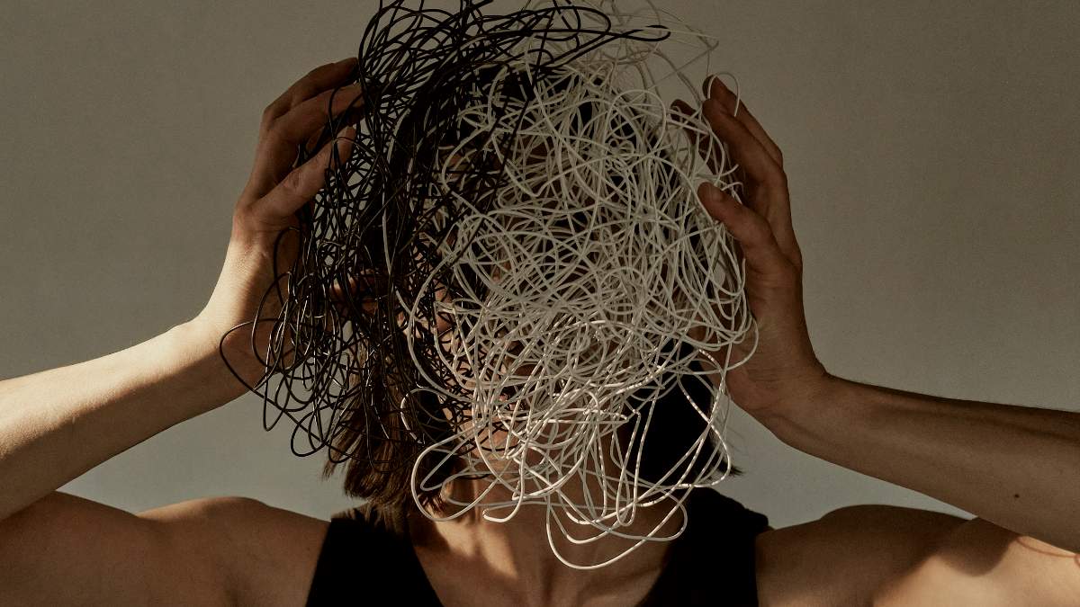 
a man holding knotted wires in front of his face to symbolize burnout
