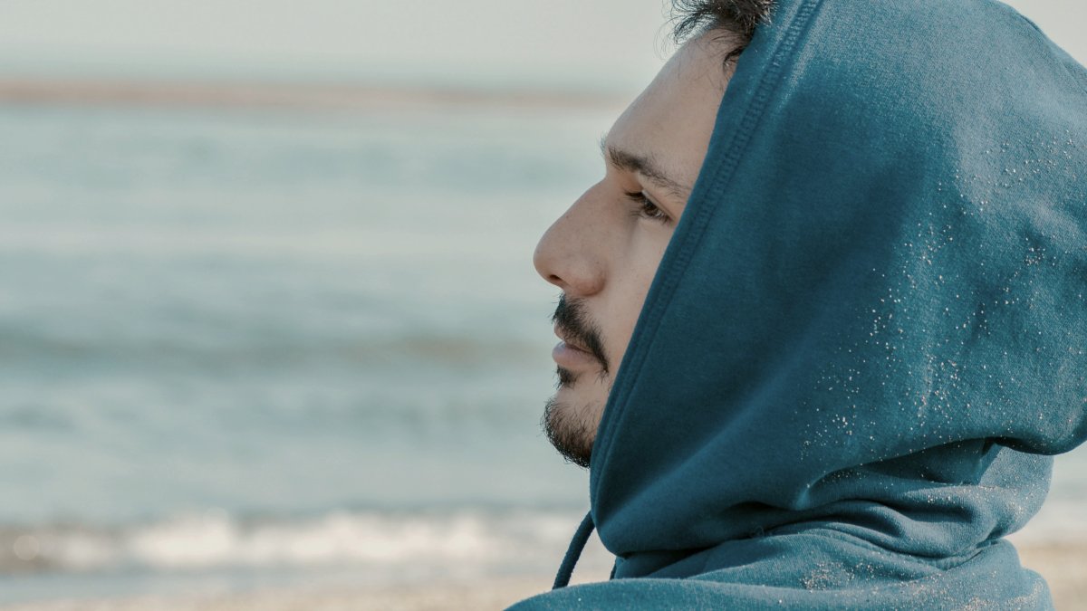 
a man in a blue hoodie sitting on a beach by Farhang Kokabian
