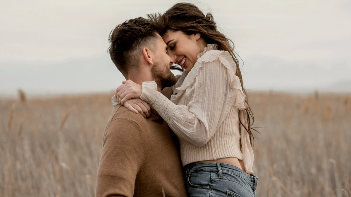 
A man in a brown sweater lovingly carries a woman in a field of tall dry grass by Micah & Sammie Chaffin
