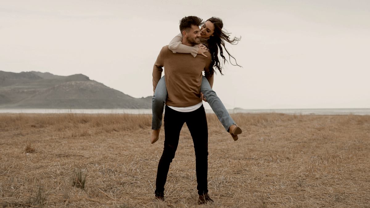 
A man piggybacking his partner in the middle of a field
