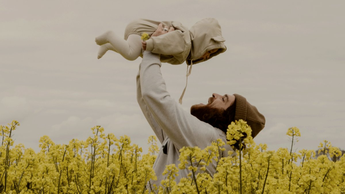 
a man raising his baby in the air in a canola field
