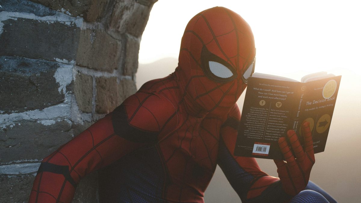 
a man reading in a spiderman costume showcasing his love and fanaticism for the character
