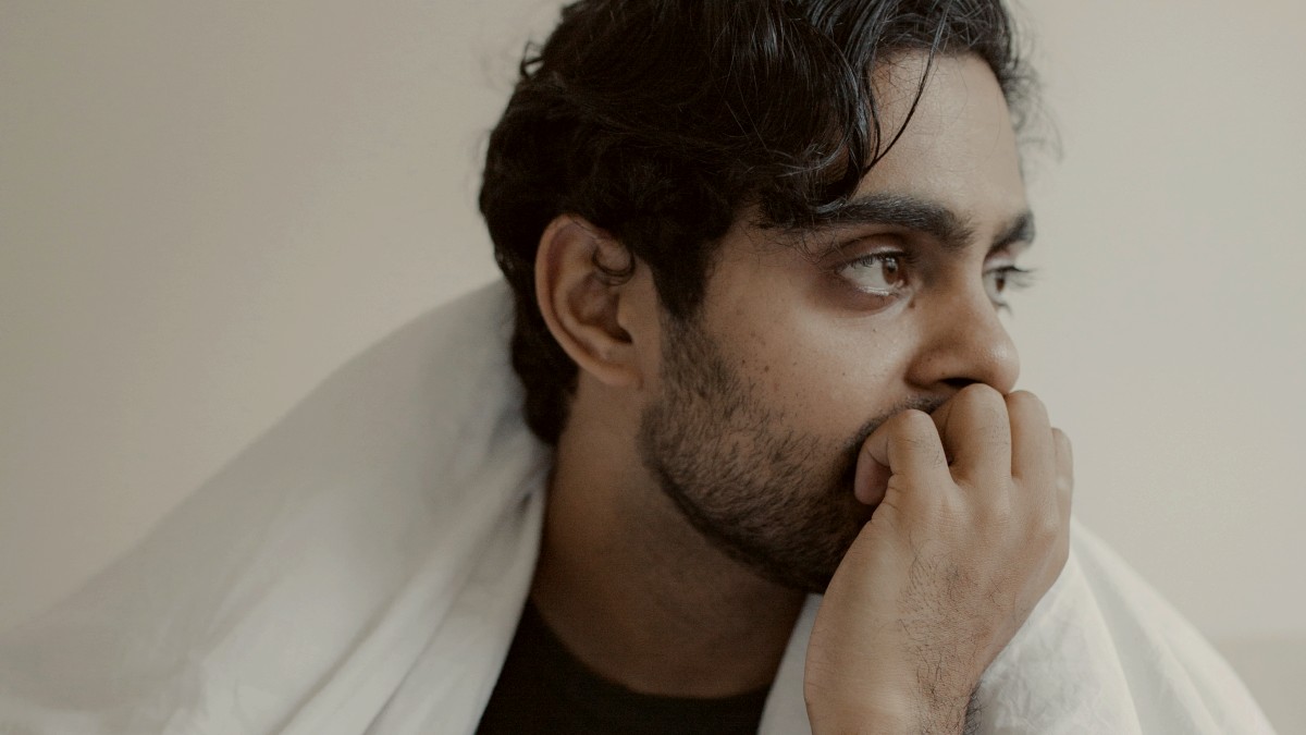 
a man sitting on a bed with a white blanket around him
