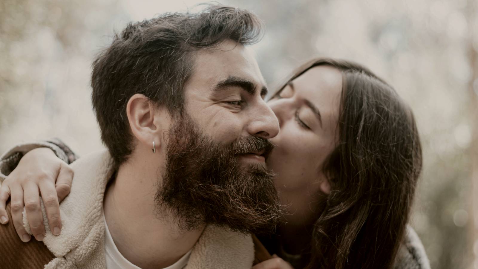 
a man with a beard and a woman are kissing in the woods by A. C.
