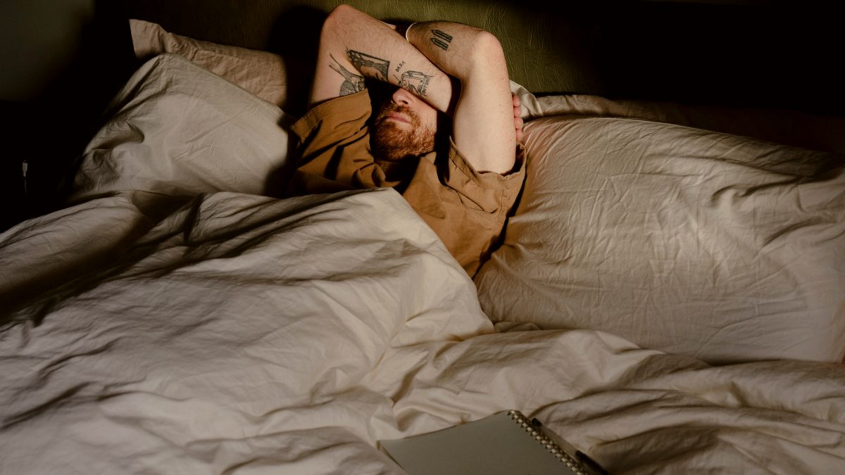 
A man with tattoos lying on a bed with a notebook nearby by Toa Heftiba
