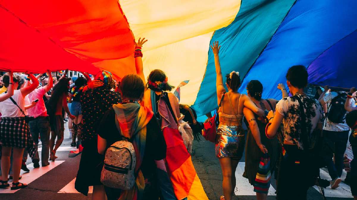 
a parade of people marching under a rainbow flag signifying allyship to the lbgt community
