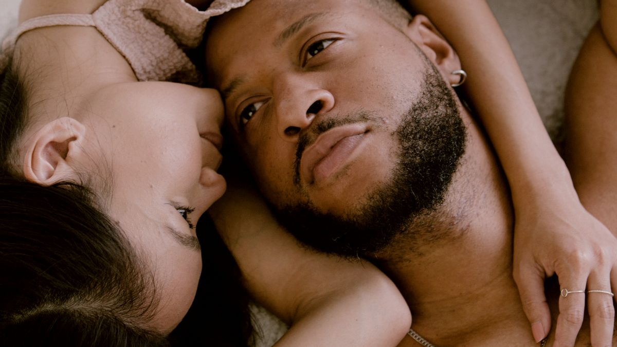 
a pensive man and a comforting woman laying on a bed together
