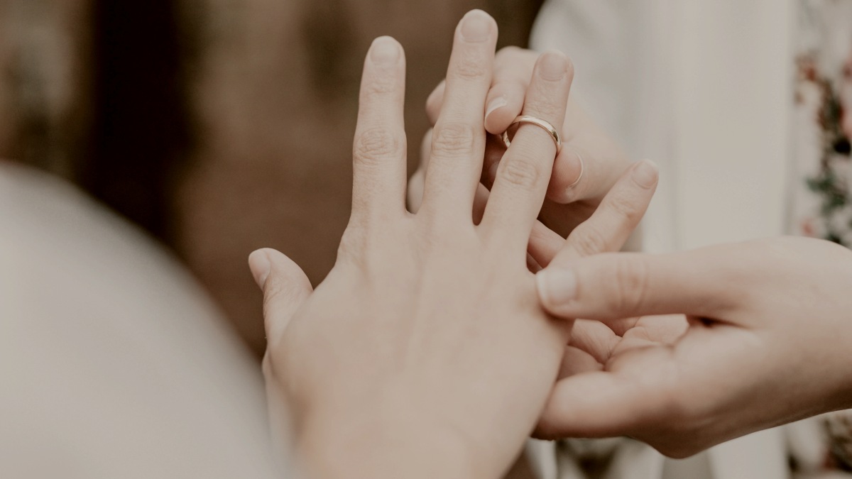 
a person holding another person's hand in a forest, placing a wedding ring on a finger by A. C.
