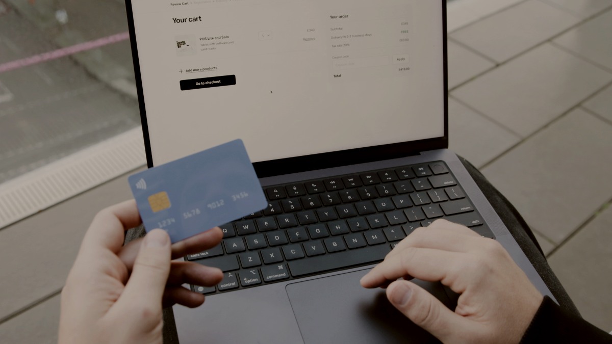 
A person sitting in a chair with a laptop and a credit card online shopping by SumUp
