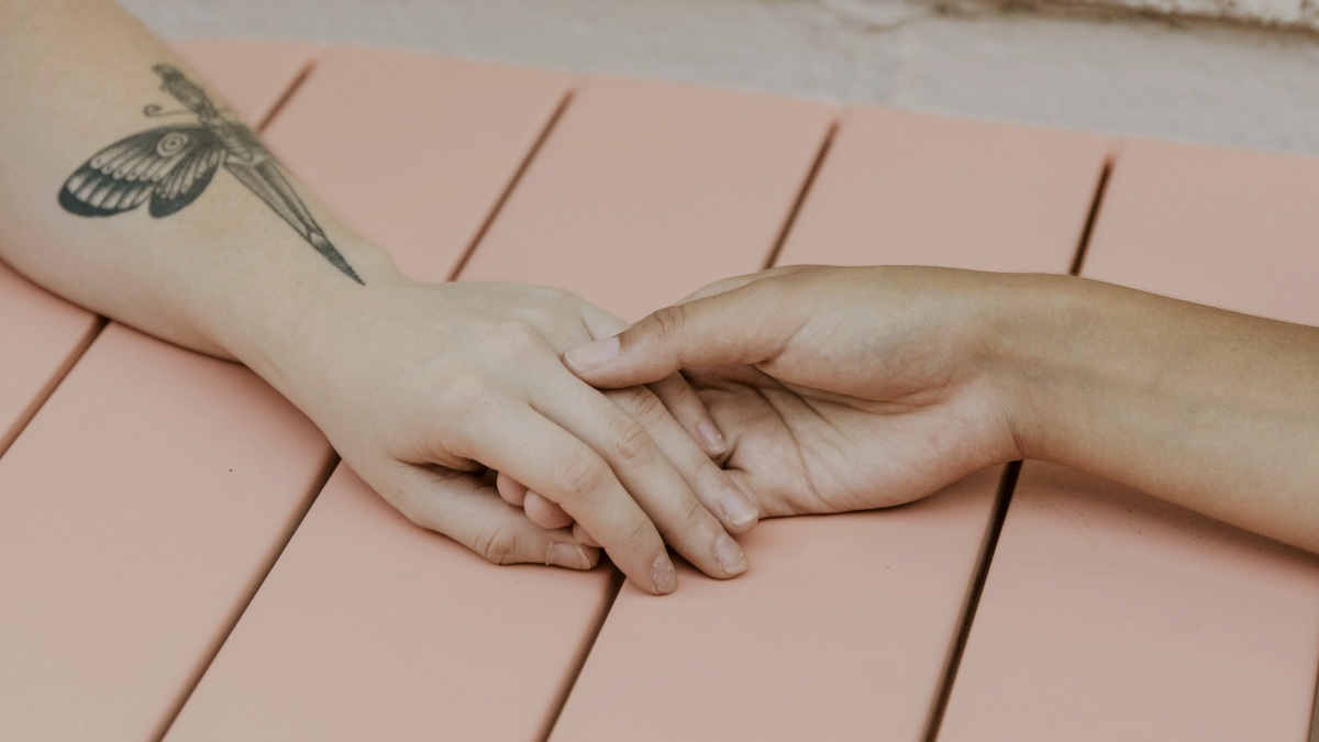 
a person with a dragonfly tattoo on their arm sitting on a pink bench holding hands with another person by tabitha turner
