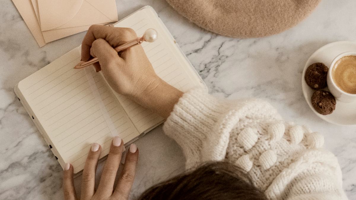 
a-person-writing-on-a-notebook-next-to-a-cup-of-coffee
