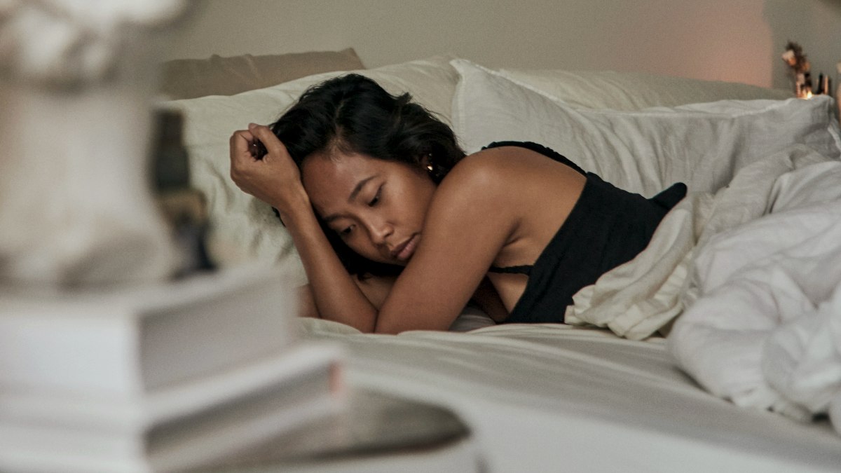 
a sad woman laying on a bed next to a vase of flowers
