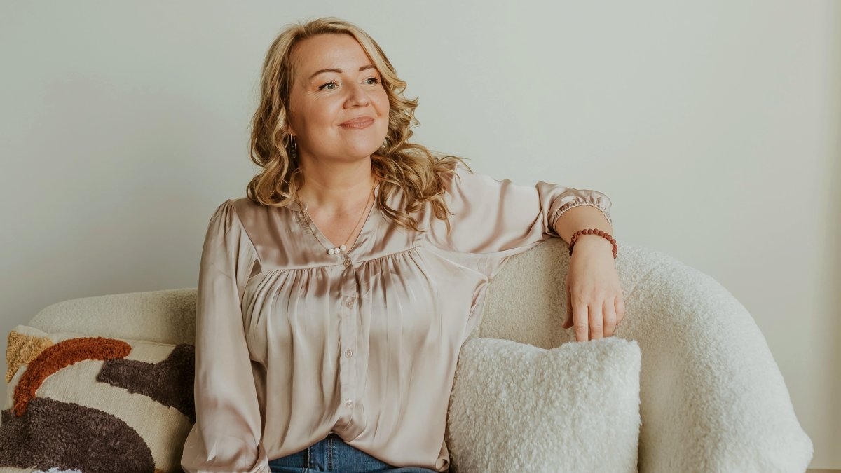 
a smiling woman sitting on top of a white couch looking into the distance
