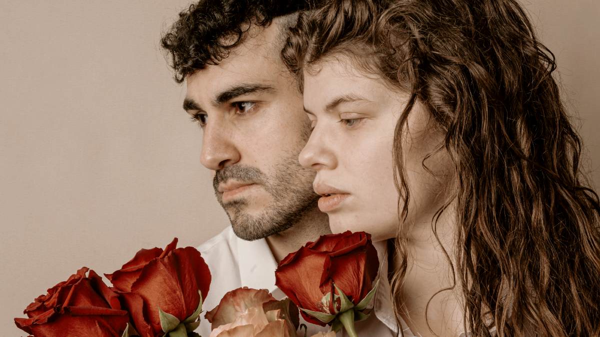 
a solemn man and woman holding a bouquet of roses together
