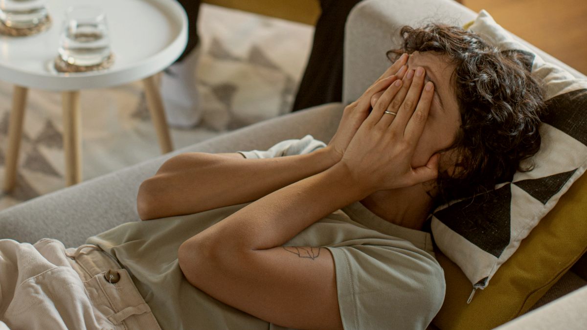 
a very stressed person laying on the couch covering their face as they cry
