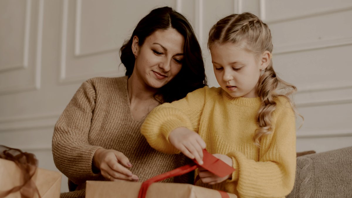 a woman and a little girl opening presents on a couch with red ribbon by Kateryna Hliznitsova